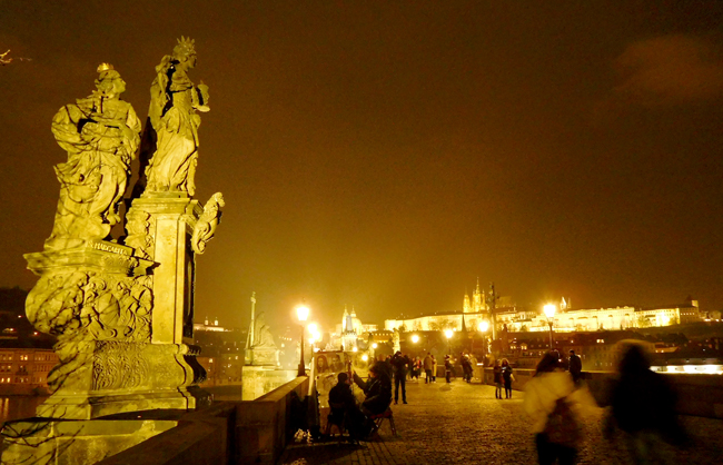 Charles Bridge lights up at night, while the Castle glows in the background.